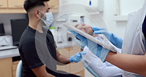 Close up caucasian female nurse typing on digital tablet while male nurse talks to patient