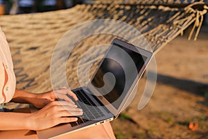 Close up caucasian female person using laptop and sitting on wicker hammock.