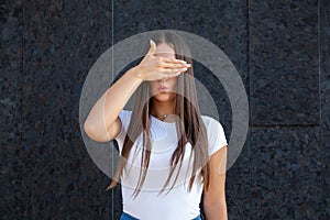 Close-up of a Caucasian girl showing duck lips, closing her eyes with her palm and dressed in a white T-shirt