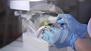 Close-up of Caucasian hands in protective gloves applying blue paint on teeth cast. Dental technician remodelling