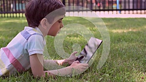 Close up Caucasian little boy using Digital Tablet sitting on the grass outdoors