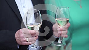 Close up of caucasian man in black suit and white shirt holding two tall glasses with white wine. Closeup of two glasses