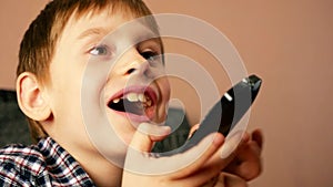 Close-up of a caucasian preschooler boy holding a TV remote control in his hand, switching programs emotionally reacts to what he