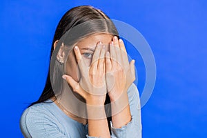 Curious Caucasian young woman closing eyes with hand and spying through fingers, hiding and peeping