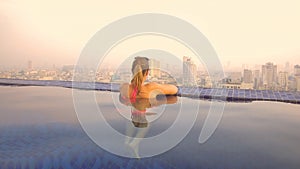 CLOSE UP: Woman enjoying a morning dip in the pool while observing the city.