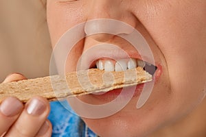 Close-up of a Caucasian woman holding a crispbread with her hand and biting it. Front three-quarter view. Low angle view