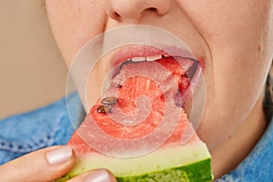 Close-up of a Caucasian woman holding a slice in her hands and eating a slice of watermelon. Front view from low angle