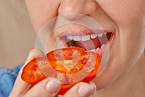 Close-up of a Caucasian woman holding a slice of sweet pepper in her hands and bringing it to her mouth. Front view from low angle