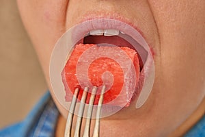 Close-up of a Caucasian woman holding a slice of watermelon on a fork and putting it in her mouth. Front view