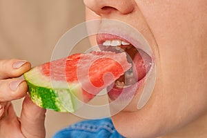 Close-up of a Caucasian woman holding a slice of watermelon in her hands and putting it in her mouth. Three-quarter front view