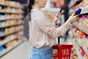 Close up of caucasian woman scan qr code of product using smartphone. Shelves with food in background. Concept of