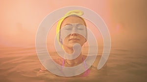 Close up caucasian woman in a swim in hot saline mineral water bath at a traditional spa outdoor with soft magic pink