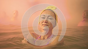Close up caucasian woman in a swim in hot saline mineral water bath at a traditional spa outdoor with soft magic pink