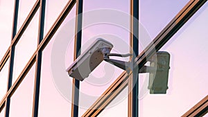 CLOSE UP: CCTV camera surveils the street near a modern building at sunset.