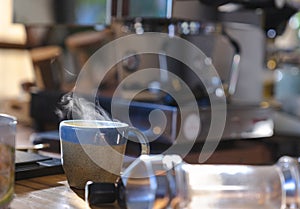 a ceramic cup of hot smoke coffee on wooden table with blurred coffee machine in background