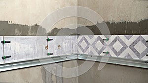 Tiler installing modern ceramic tiles on bathroom wall using tile leveling system