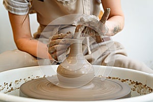 close up of ceramist hands working and ceramic vase on the lathe or potter's wheel inside a pottery workshop with natural