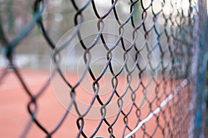 Close-up on a chain-link fence with a tennis court in the background.