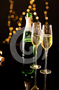 Close up of champagne in flutes with bottle reflecting on glass table