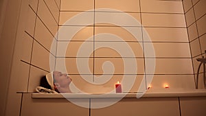 Close-up of a charming African American woman taking a relaxing bubble bath by the light of scented red candles. Cleanliness, hygi