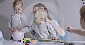 Close-up of charming Caucasian little girl sitting at the table with mother, sister and brother. Happy family resting