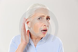 Close-up of charming elderly woman, holding hand by her ear and