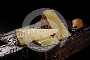 Close-up of Cheddar cheese. Semi-soft aged cows milk cheese according to an old English recipe. Piece of cheese on a dark wooden