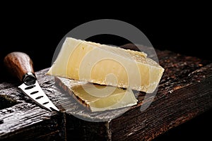 Close-up of Cheddar cheese. Semi-soft aged cows milk cheese according to an old English recipe. Piece of cheese on a dark wooden