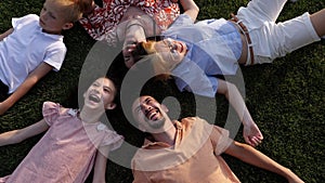 Close-up of a cheerful big family lying down together on the grass in a circle.