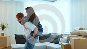 Close up of cheerful Caucasian man and woman having fun playing in new house on moving day. Piggyback ride. Happy young