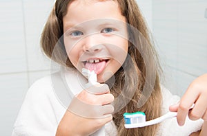 Close-up, a cheerful girl with long hair, holding a toothbrush in her hand and fooling around, trying to taste the paste