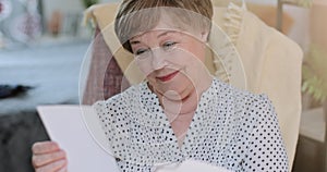 Close up of cheerful grandmother looking at family photos while sitting on chair. Emotional good looking retired female