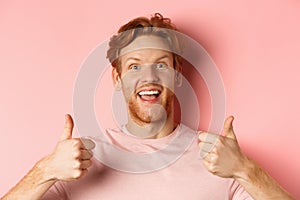 Close up of cheerful man with red hair and beard, showing thumbs up and smiling, saying yes, approve and praise