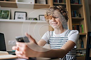 Close-up of cheerful preteen girl holding and using smartphone, browsing social network apps, surfing internet and