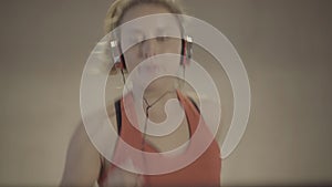 Close-up of cheerful sportswoman jogging on treadmill and looking at camera. Portrait of young blond beautiful Caucasian
