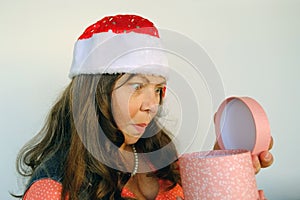 Close-up cheerful surprised adult woman in santa claus red hat holding round pink box with gift, festive mood, congratulations,