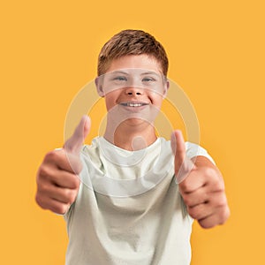 Close up of cheerful teenaged disabled boy with Down syndrome smiling at camera, showing thumbs up while standing