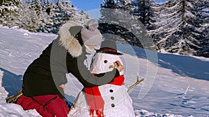 CLOSE UP: Cheerful young woman is building a snowman on a sunny winter day.