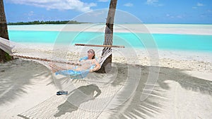 CLOSE UP: Cheerful young woman relaxing under the palms in a comfortable hammock