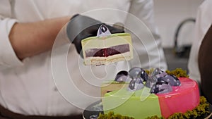 A close-up of a chef in gloves cutting a mousse cake with a green mirror glaze.