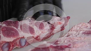 Close-up of a chef in gloves cutting pork ribs with a knife on a cutting board.