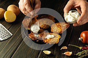 Close-up of a chef hands adding sour cream to fried potato pancakes with a spoon. Concept of preparing delicious food in a hotel