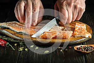 Close-up of a chef hands cutting fresh red salmon fish with a knife on a kitchen cutting board. Cooking a delicious fish dish