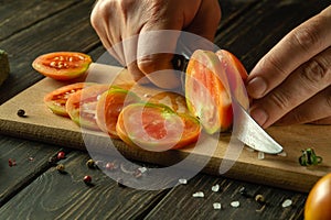 Close-up of a chef hands with a knife cutting a tomato into small pieces for a vegetable salad. Work environment on the kitchen