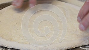 Close-up of the chef rolling out a round pizza dough with his hands.