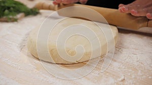 Close up of the chef's female hands roll the dough with a wooden rolling pin.