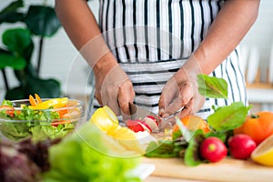 Close-up of chef`s hand using stainless steel knife to cut radishes on a wooden cutting board