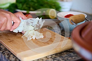 Close-up chef's hands chopping onion on wooden cutting board, preparing dinner at home