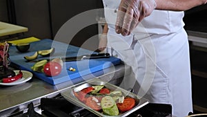 Close-up of a chef salting grilled vegetables in a professional kitchen.