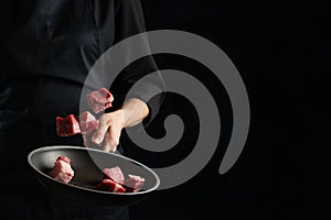 Close-up of chef throwing fresh beef meat in frying pan on black background. Preparing dish with meat. Frozen notion. Food concept